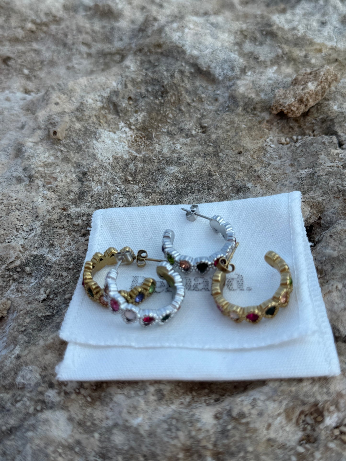 Pair of hoop earrings with gemstones on a white card against a stone background