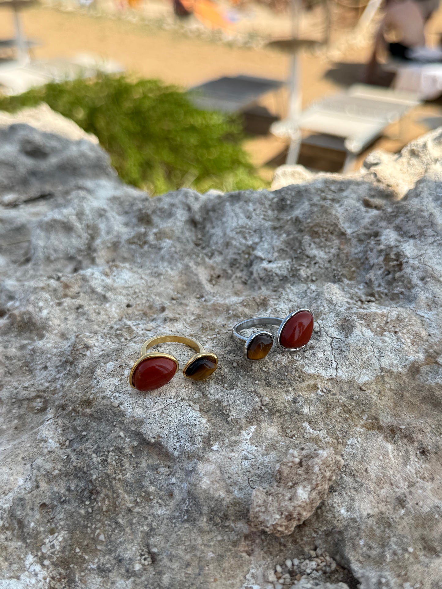 Two rings with red stones on a textured stone surface with a blurred outdoor background.