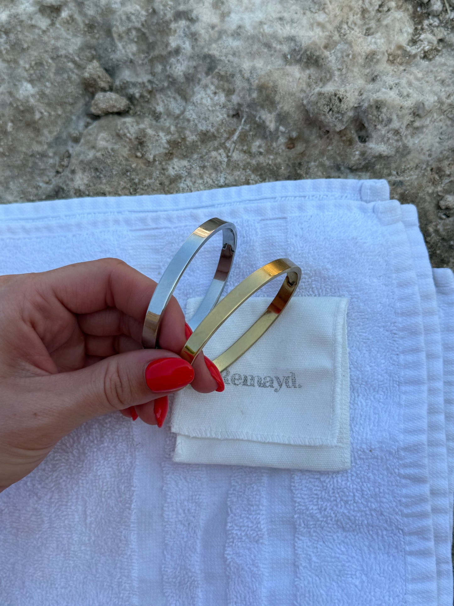 Hand holding two bangles over a white cloth with 'Kennedy' branding on a stone surface.