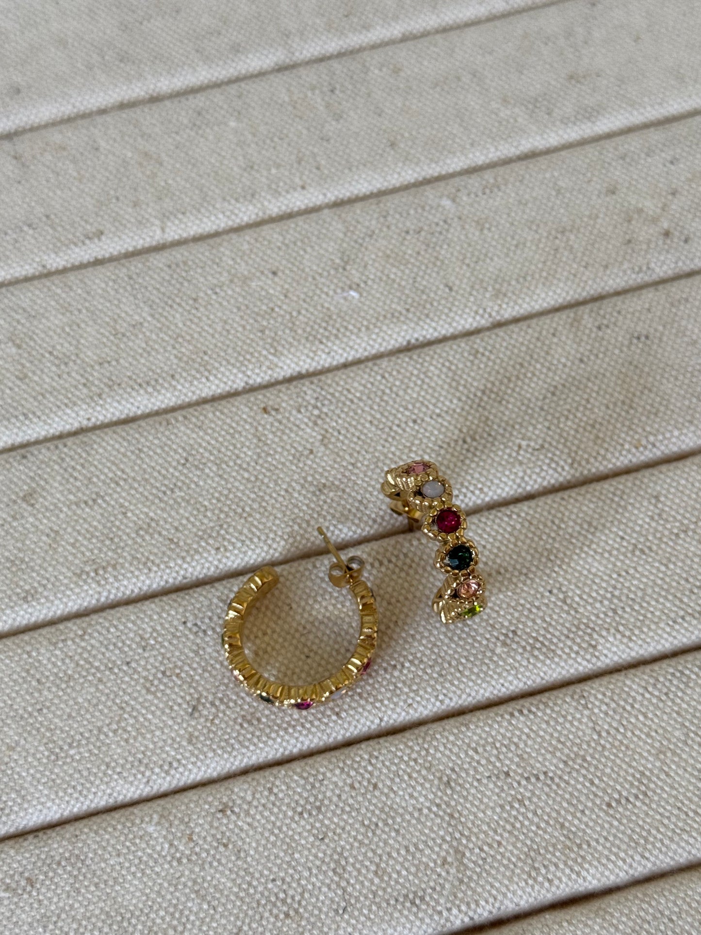 Gold hoop earrings with gemstones on a beige wooden surface