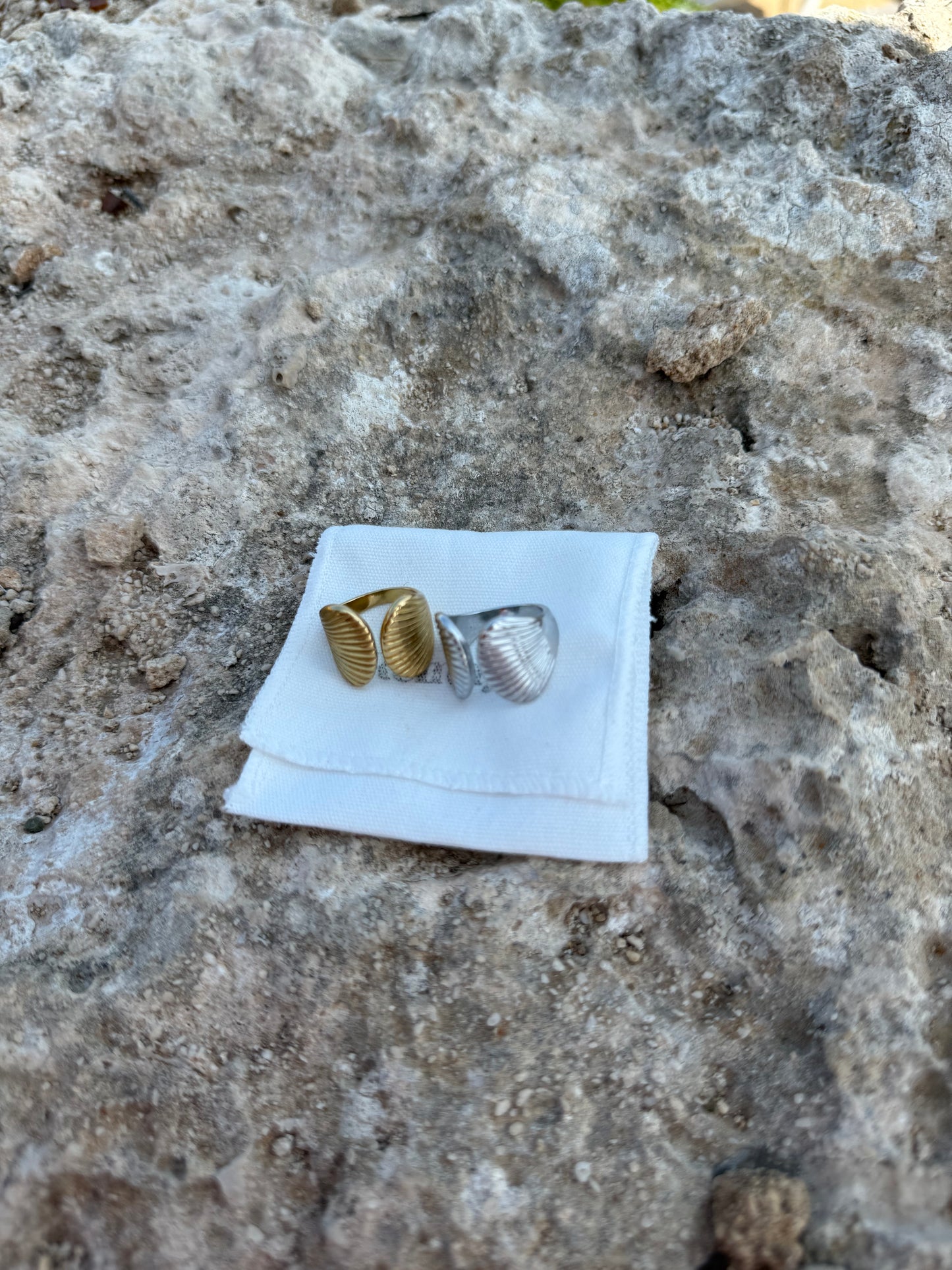 Two shell-shaped rings on a white JEWELLERY BAG against a textured stone background