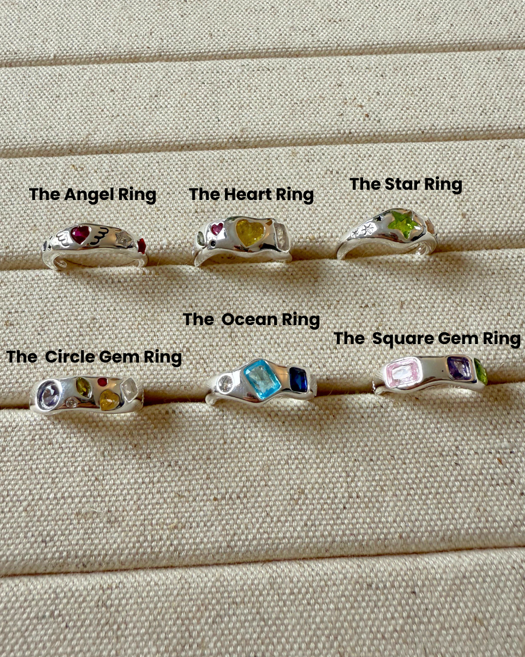 Set of six silver rings with gemstones on a textured beige surface