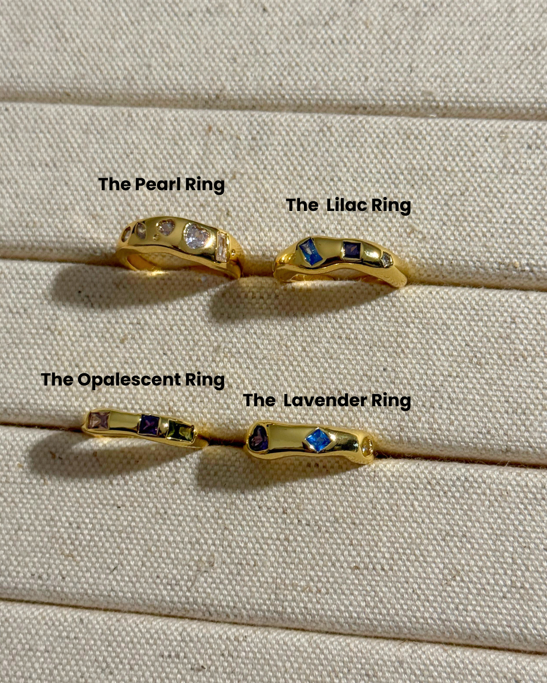 Four gold rings labeled 'The Pearl Ring', 'The Lilac Ring', 'The Opalescent Ring', and 'The Lavender Ring' on a textured beige surface.