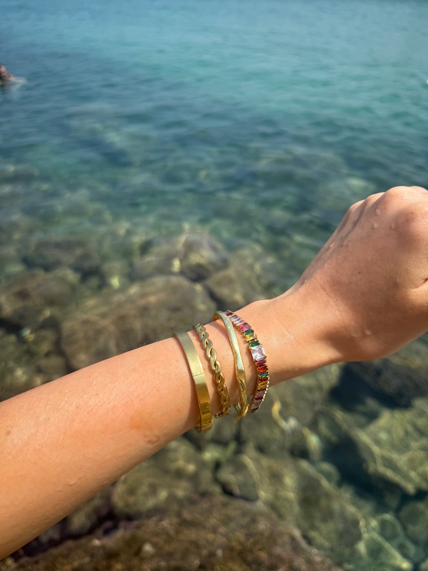 Arm with gold bracelets against a blurred natural background