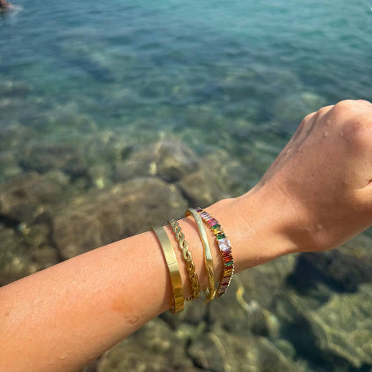 Arm with gold bracelets against a blurred natural background