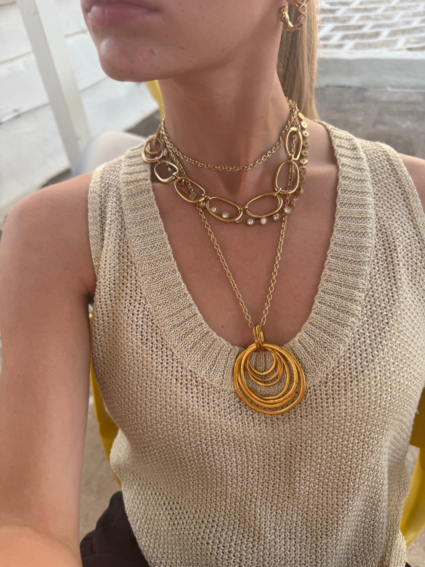 Woman wearing a beige sleeveless top with layered gold necklaces.