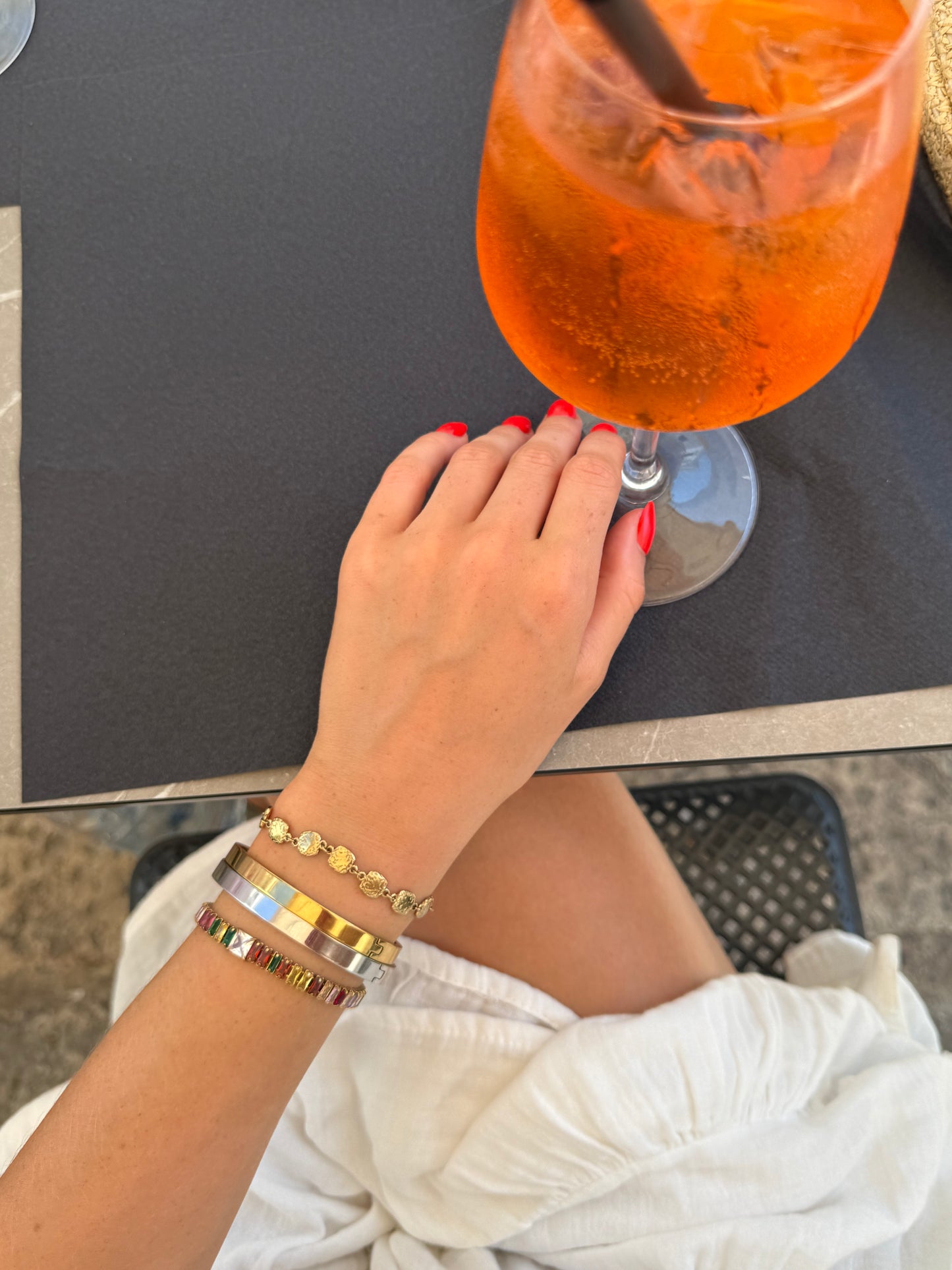 Hand with colorful bracelets holding an orange drink on a table