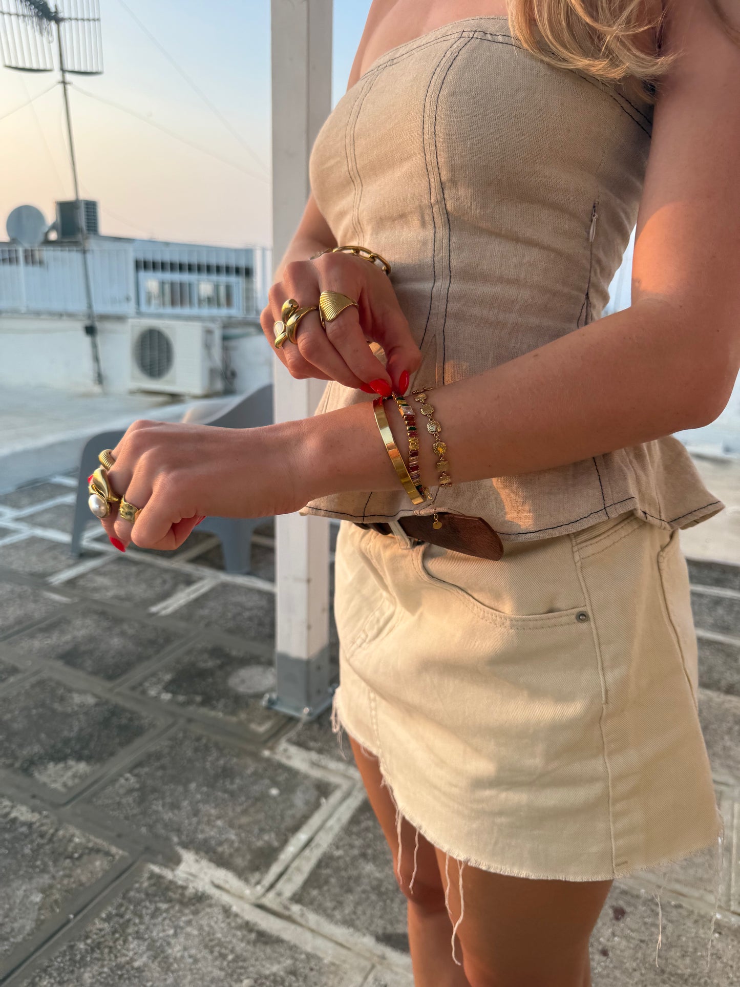 Person wearing a beige strapless top and skirt with multiple bracelets and rings on a paved area.