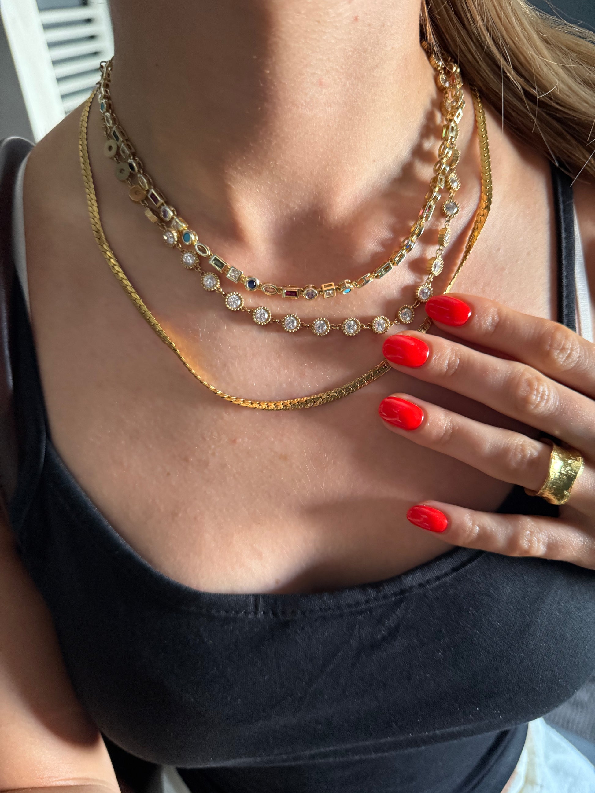 Close-up of a person wearing multiple necklaces with a hand touching the chest.