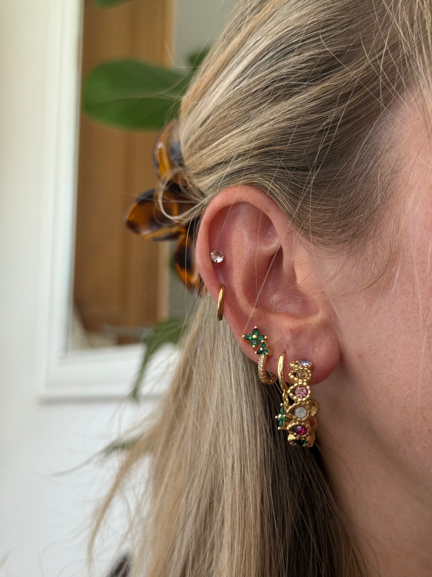 Close-up of a person wearing gold hoop earrings with gemstones indoors.