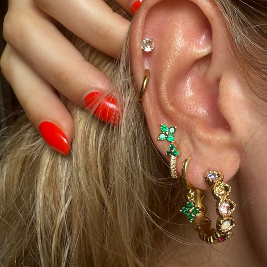 Close-up of an ear with multiple earrings and a hand adjusting hair.