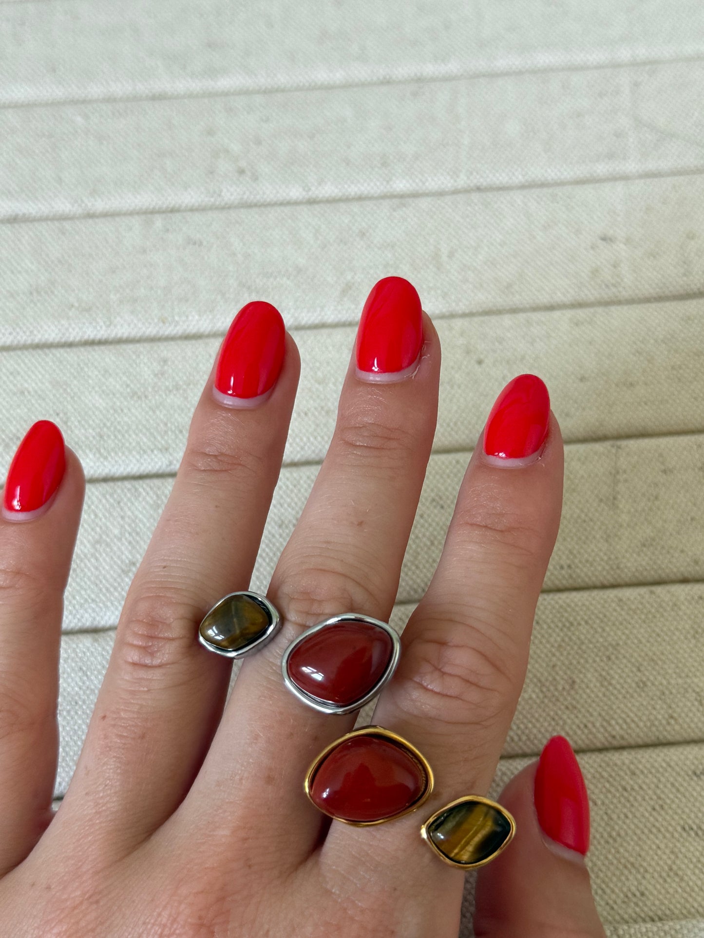 Hand wearing three rings with red gemstones on a light background