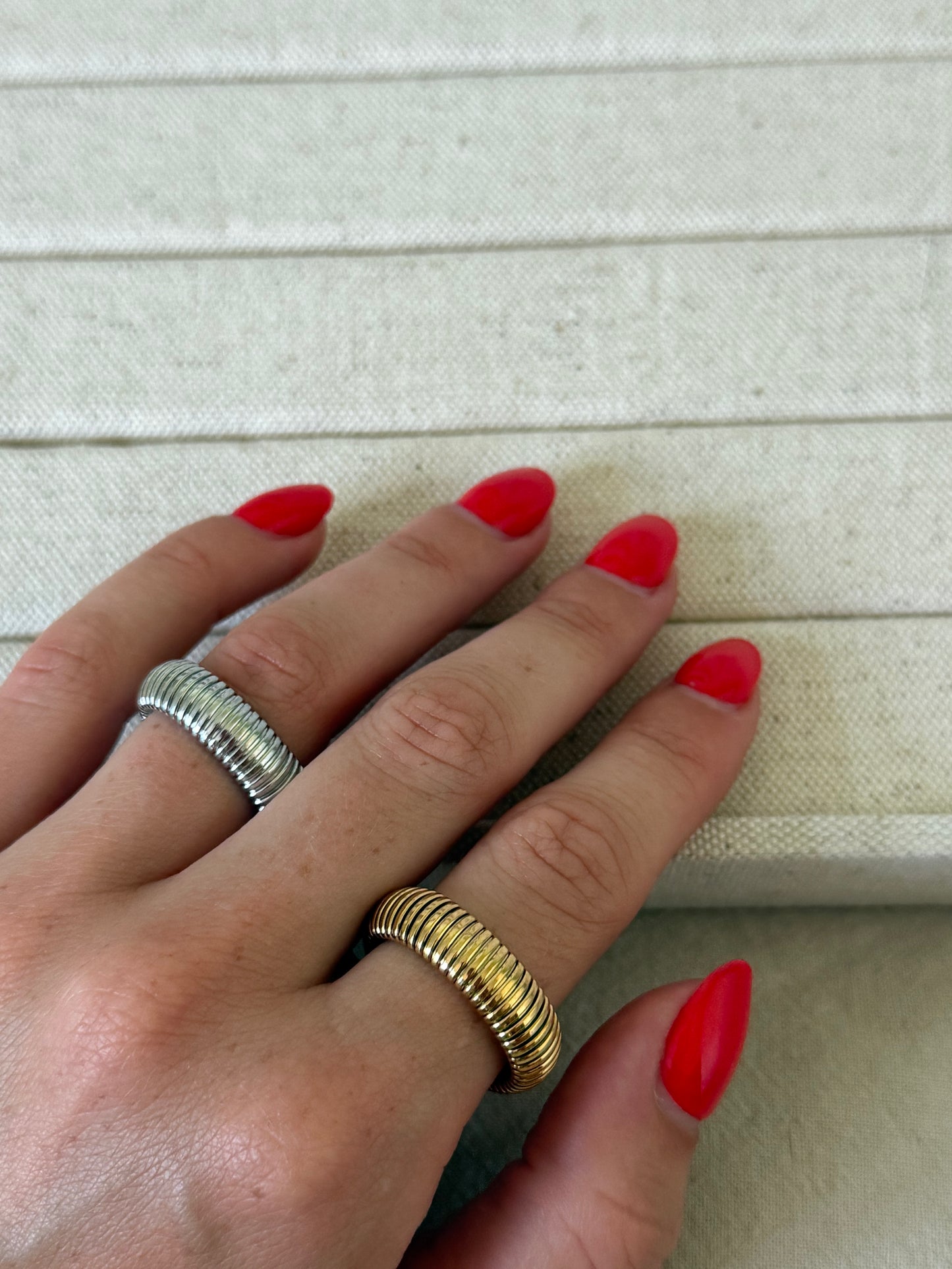Hand with red nail polish wearing two rings on a light background