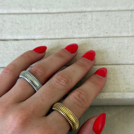 Hand with red nail polish wearing two rings on a light background