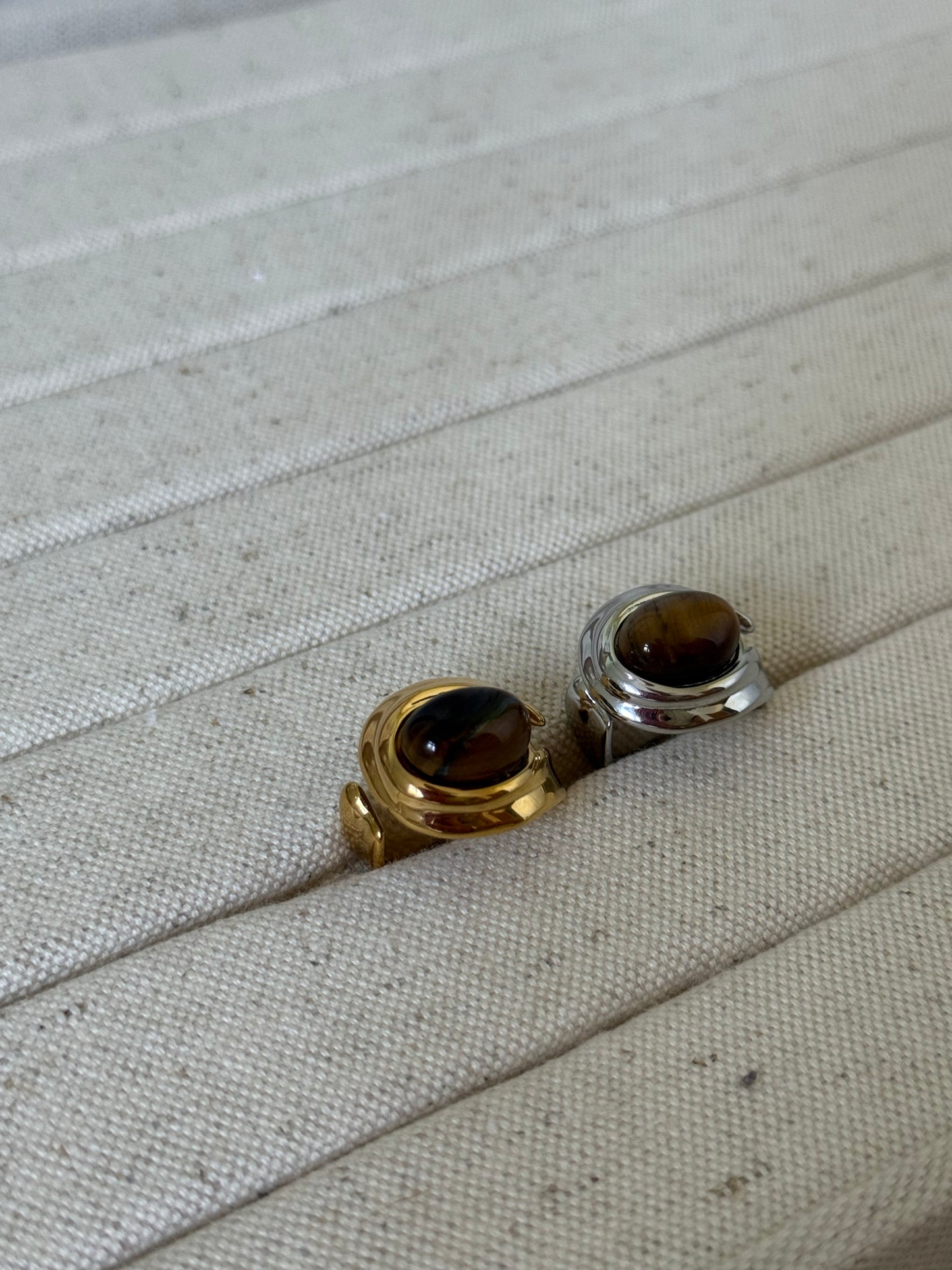 Two rings with brown gemstones on a textured beige surface