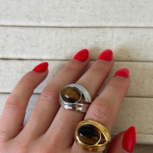 Hand wearing two rings with tiger's eye stones on a neutral background