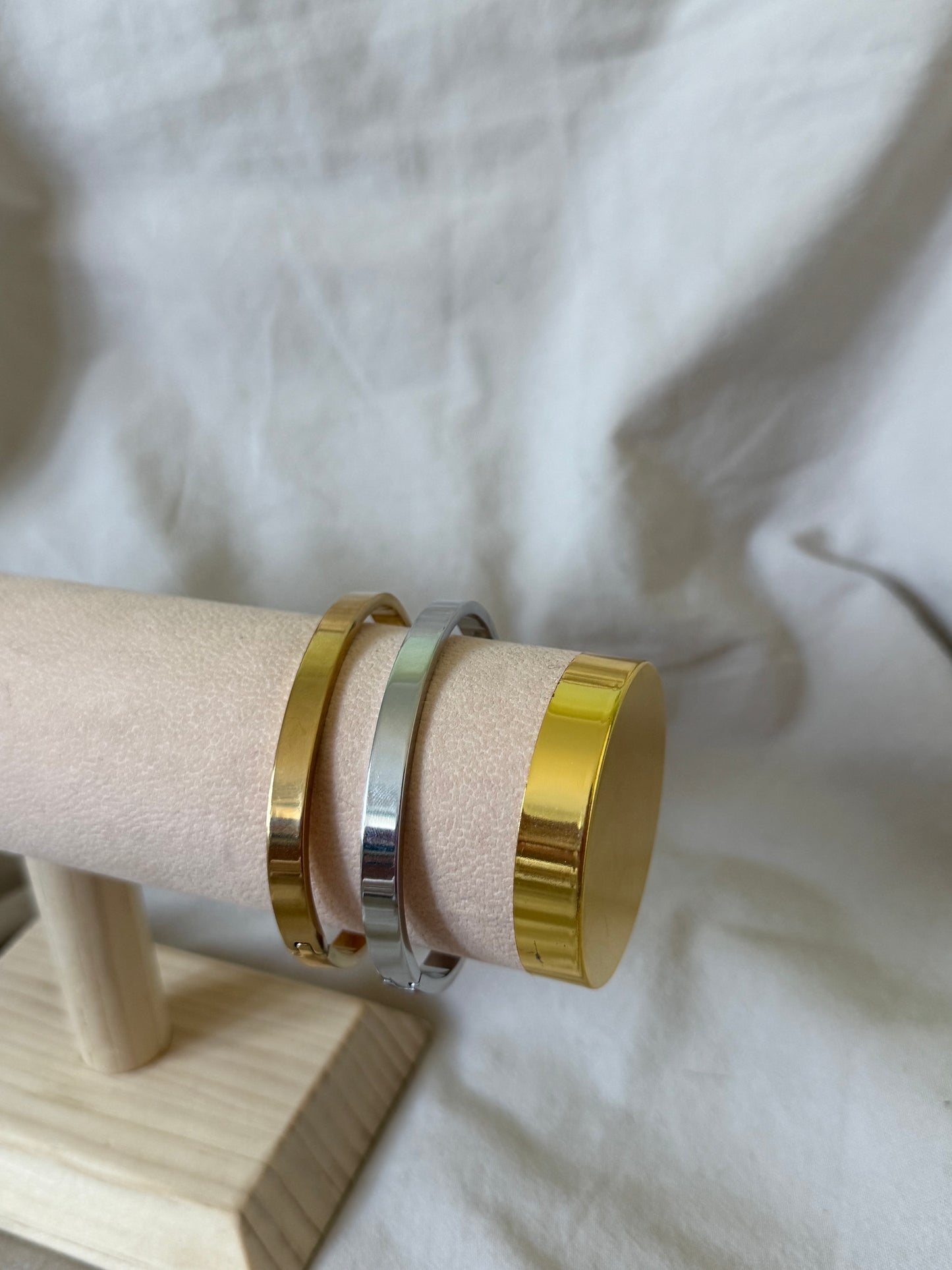 Two gold and silver bangles on a wooden stand with a white fabric background