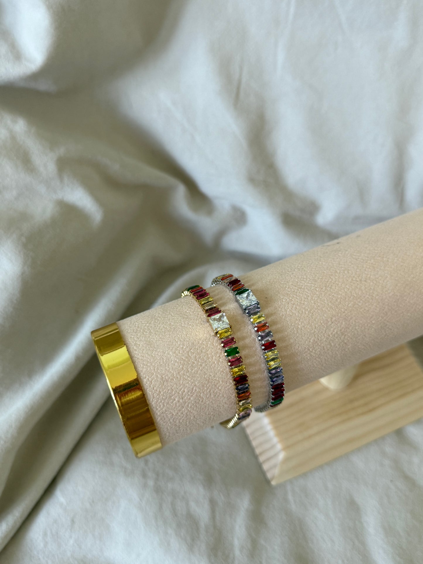Multicolored beaded bracelet on a wrist with a gold ring, against a white fabric background