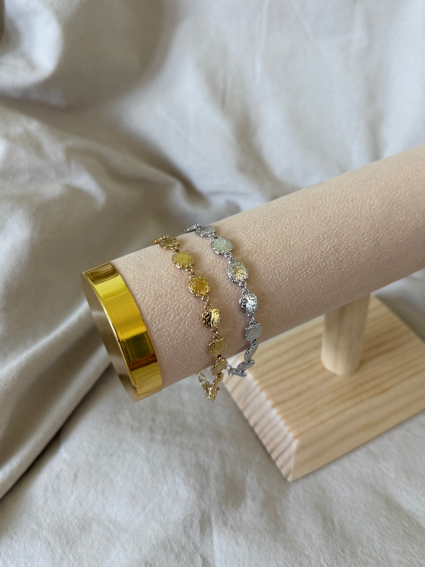 GOLD SILVER bracelets on a wooden stand against a white fabric background
