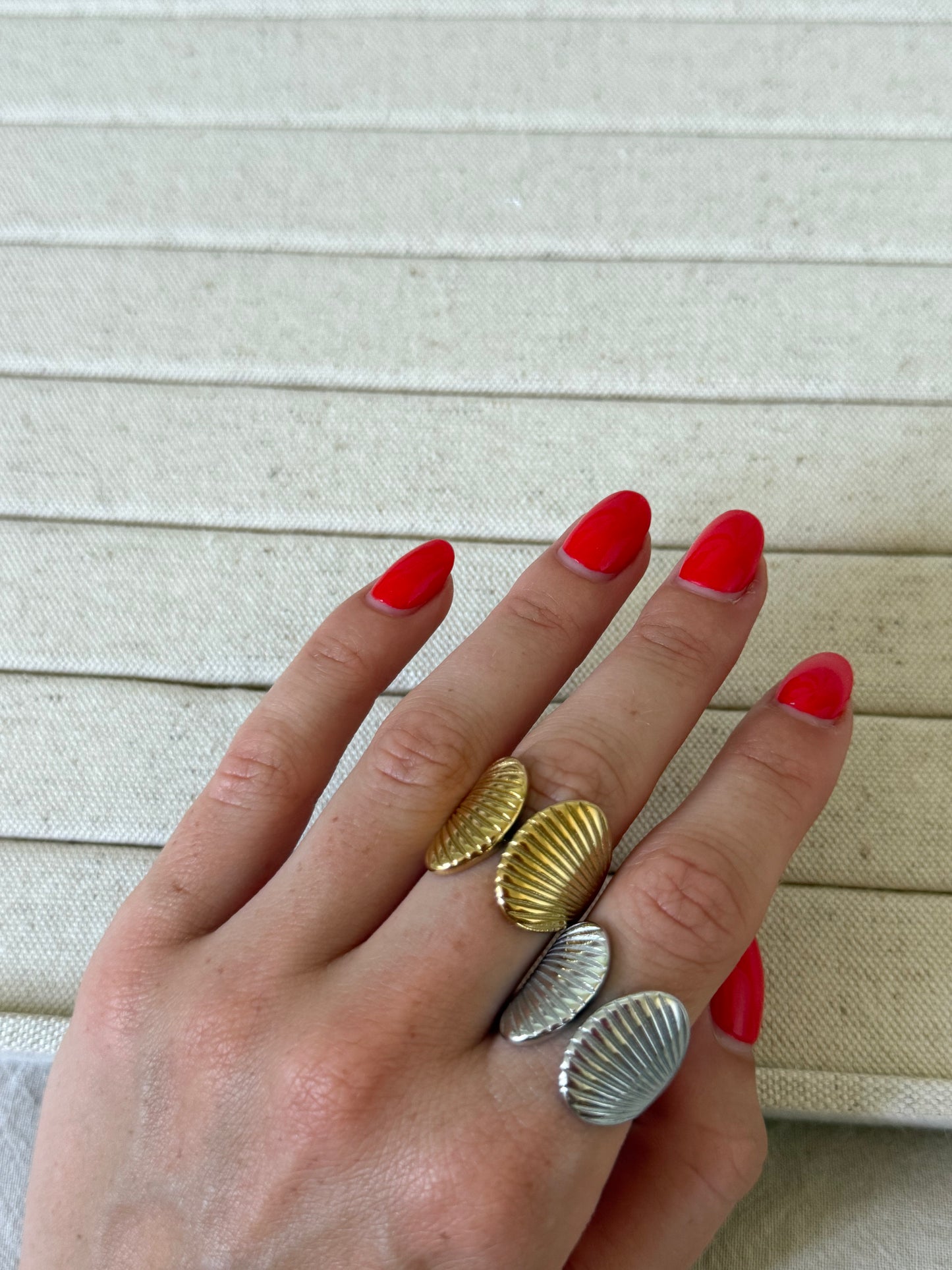 Hand wearing three shell-shaped rings on a beige fabric background