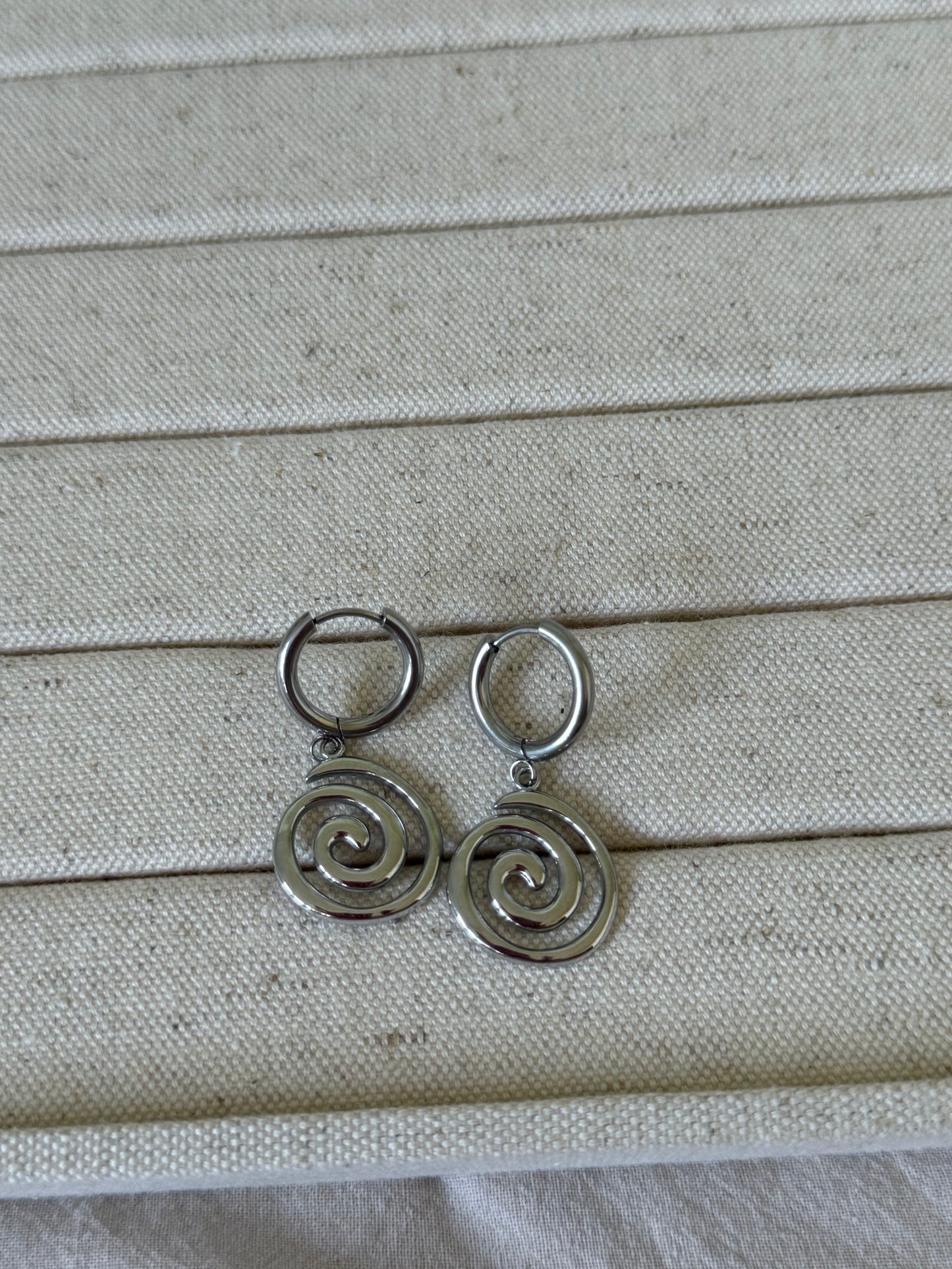 Silver spiral earrings on a textured beige fabric background