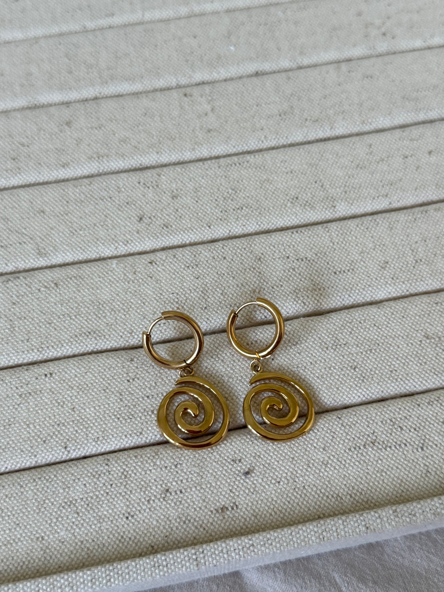 Gold spiral earrings on a textured beige fabric background