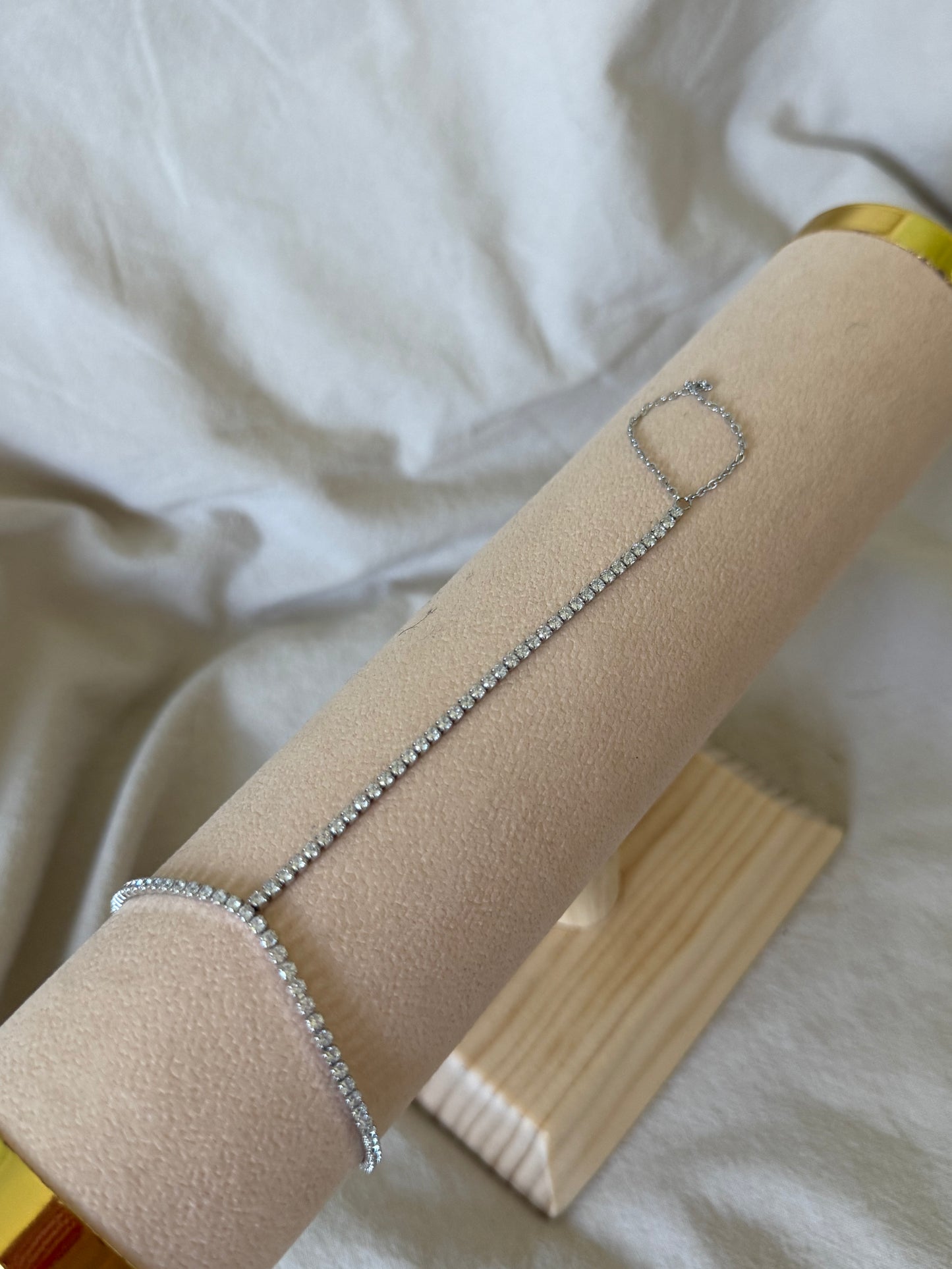Silver bracelet/HAND CHAIN on a beige cylindrical display with a white fabric background