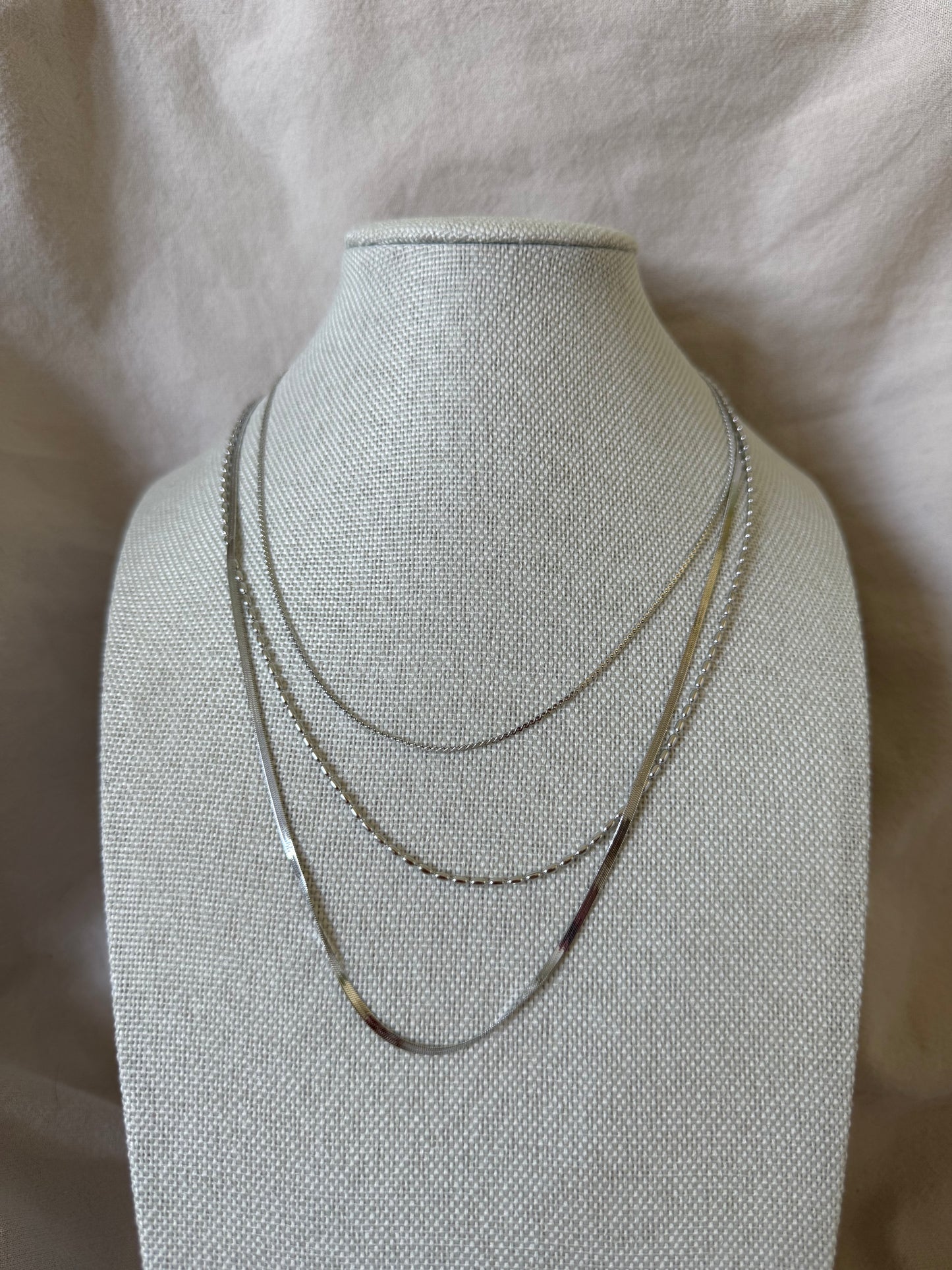 Three thin gold necklaces on a gray mannequin bust against a light background