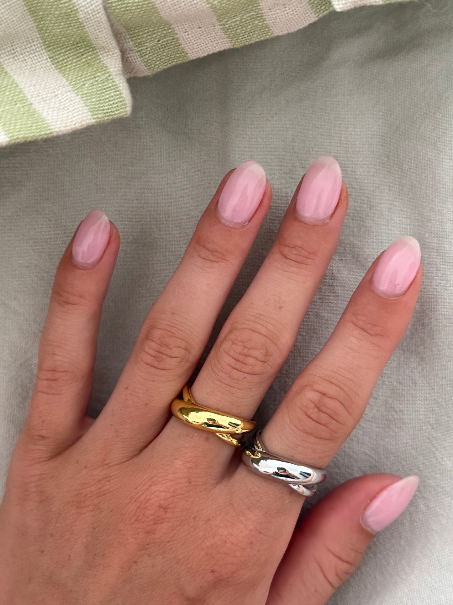 Hand wearing two rings with pink nail polish on a neutral background