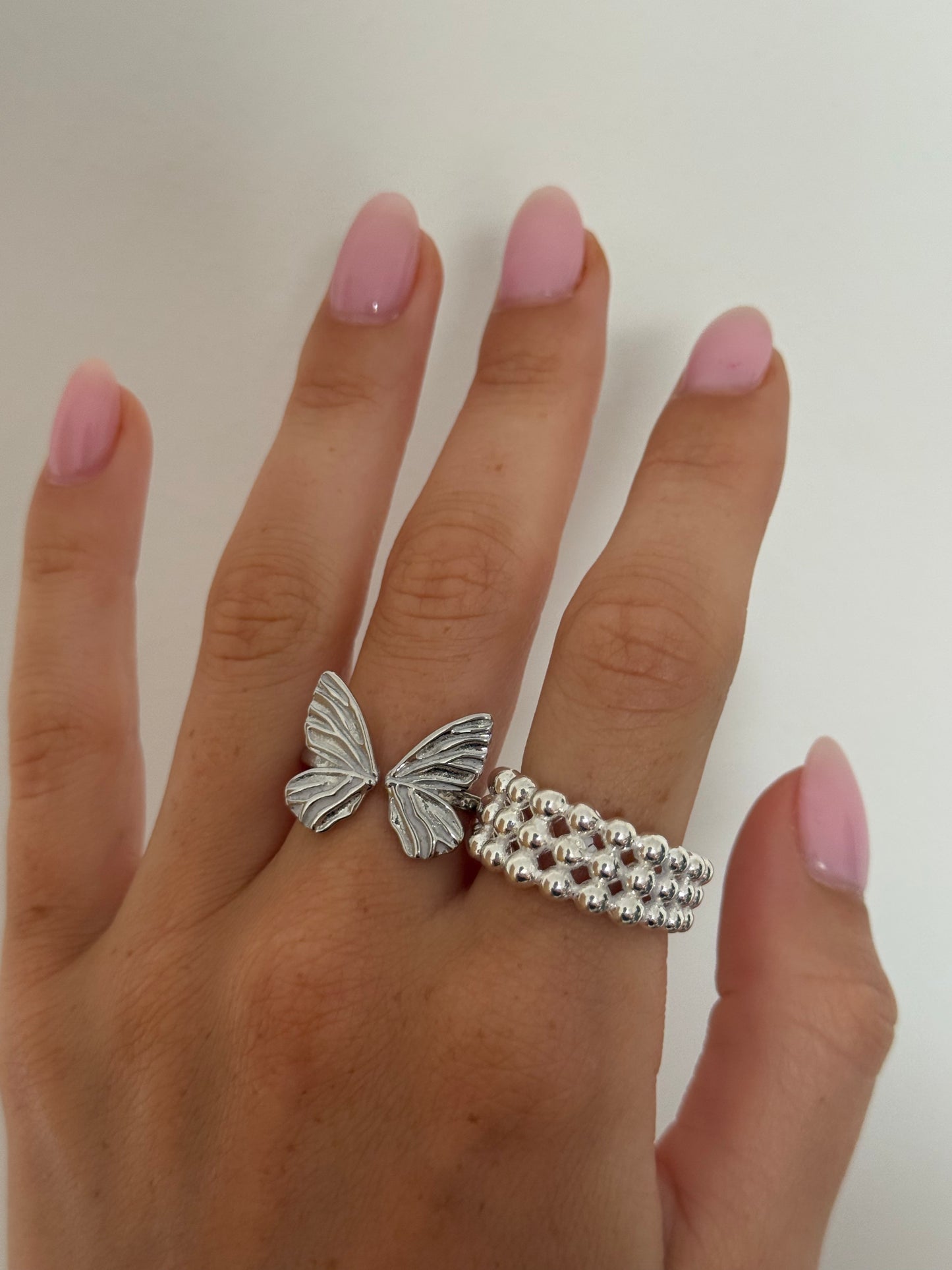 Silver butterfly ring on a finger with a plain background