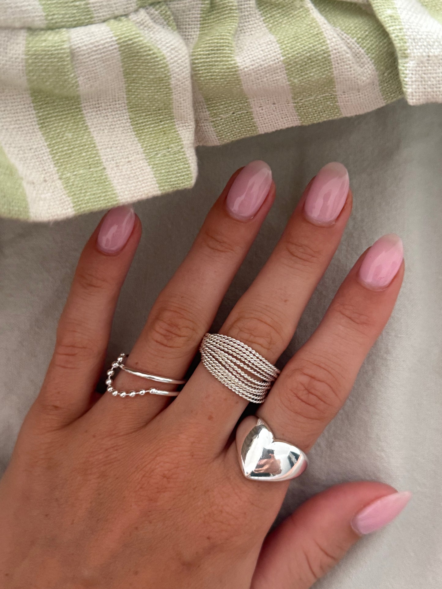 Hand with multiple silver rings on a neutral background