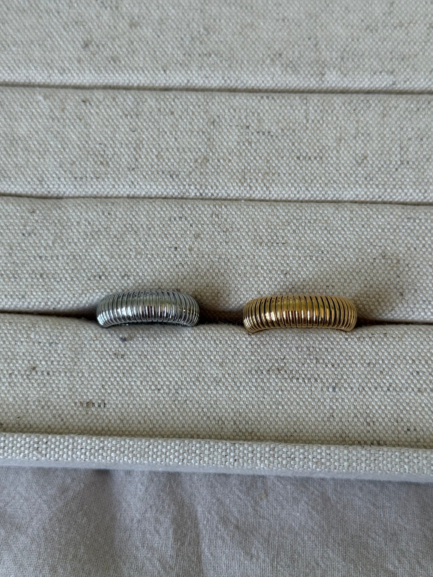 Two rings, one silver and one gold, on a textured surface.