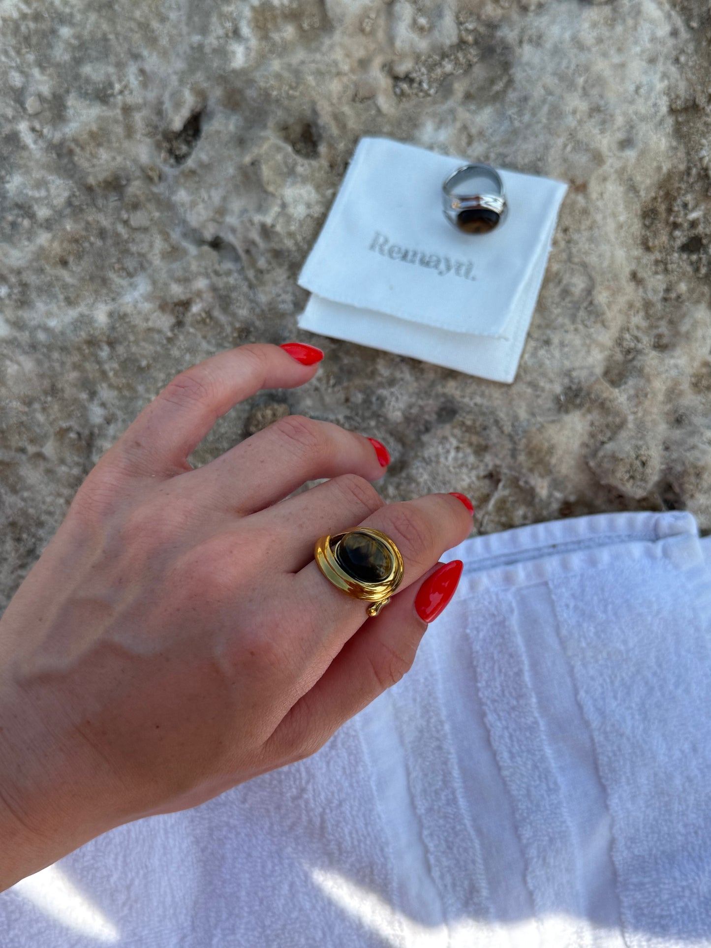 Hand wearing a gold ring with a dark stone, with a branded card in the background.