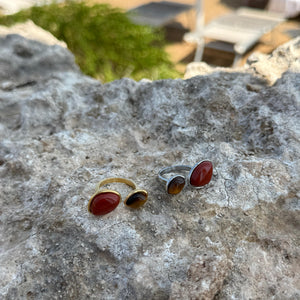 Two rings with red stones on a textured stone surface with a blurred outdoor background.
