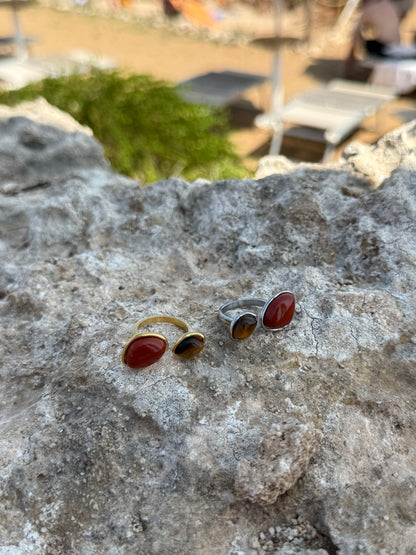 Two rings with red stones on a textured stone surface with a blurred outdoor background.