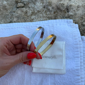 Hand holding two bangles over a white cloth with 'Kennedy' branding on a stone surface.