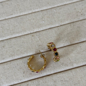 Gold hoop earrings with gemstones on a beige wooden surface