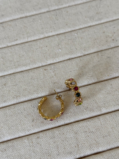 Gold hoop earrings with gemstones on a beige wooden surface