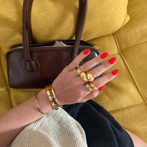 Hand with red nails and gold jewelry holding a brown handbag on a yellow couch.