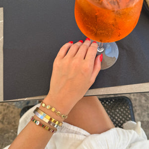 Hand with colorful bracelets holding an orange drink on a table