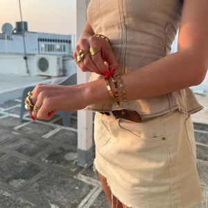 Person wearing a beige strapless top and skirt with multiple bracelets and rings on a paved area.