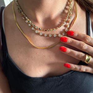 Close-up of a person wearing multiple necklaces with a hand touching the chest.