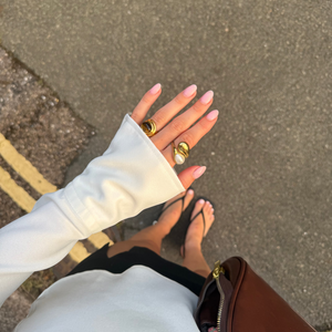 Close-up of a person's hands with white gloves and gold rings on a concrete surface.