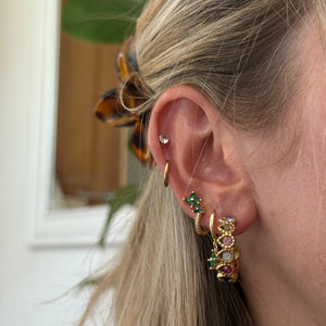 Close-up of a person wearing gold hoop earrings with gemstones indoors.