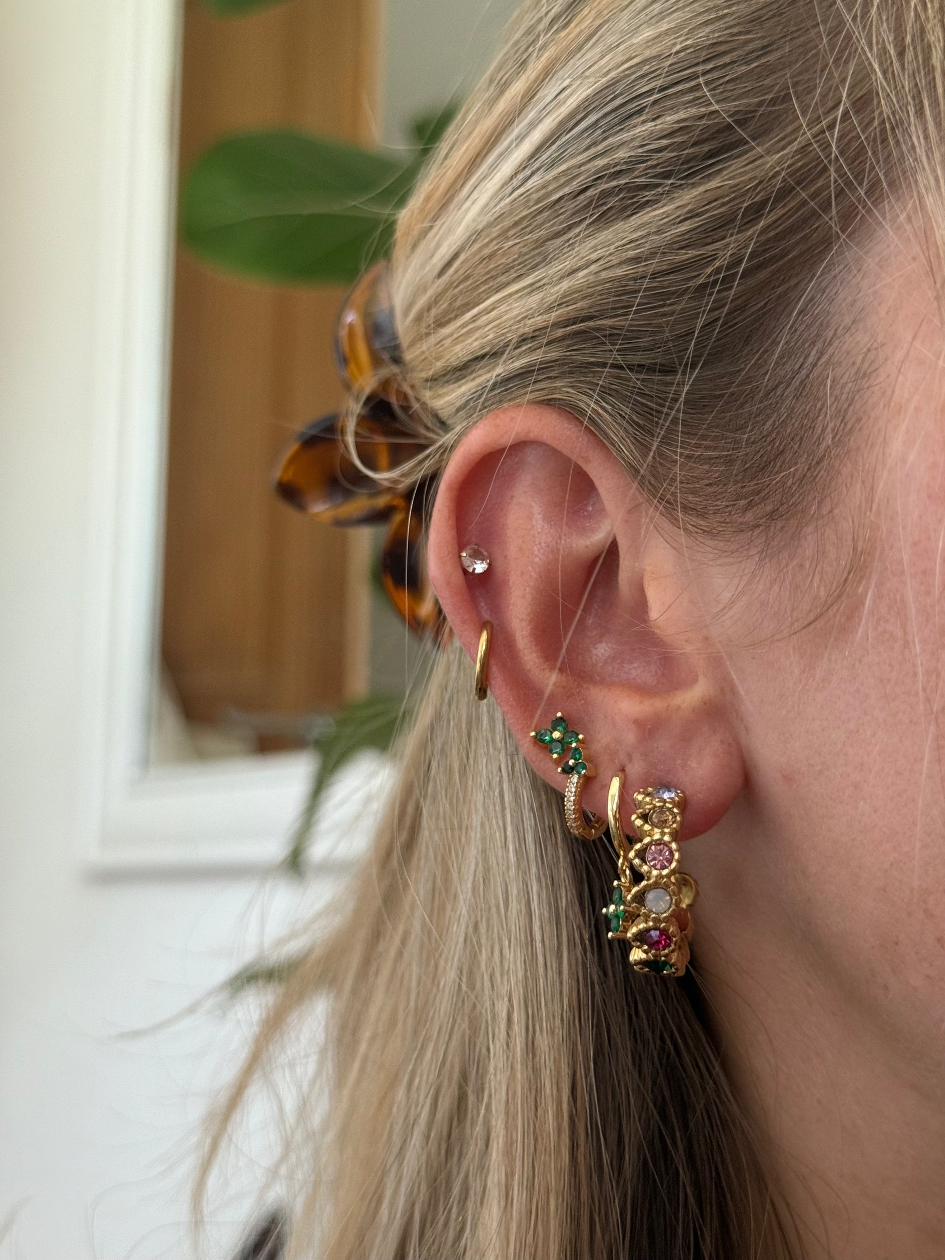 Close-up of a person wearing gold hoop earrings with gemstones indoors.