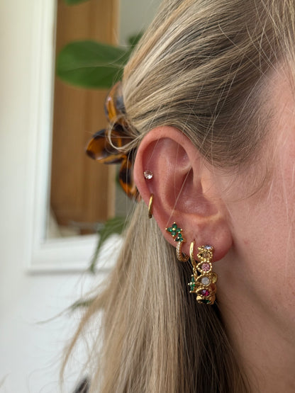 Close-up of a person wearing gold hoop earrings with gemstones indoors.