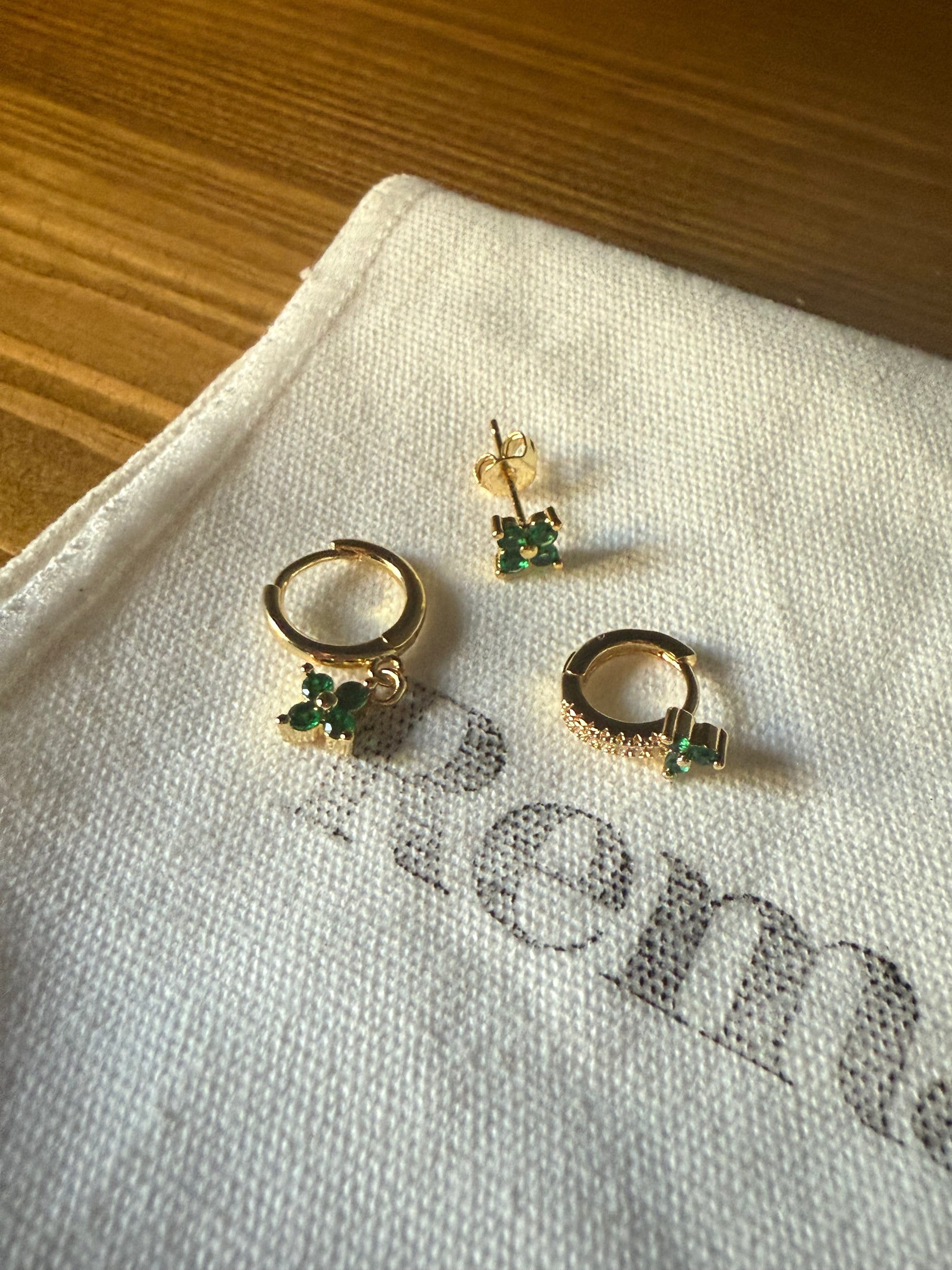 Gold and green earrings on a white cloth with REMAYD branding.