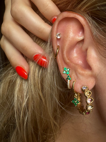 Close-up of an ear with multiple earrings and a hand adjusting hair.