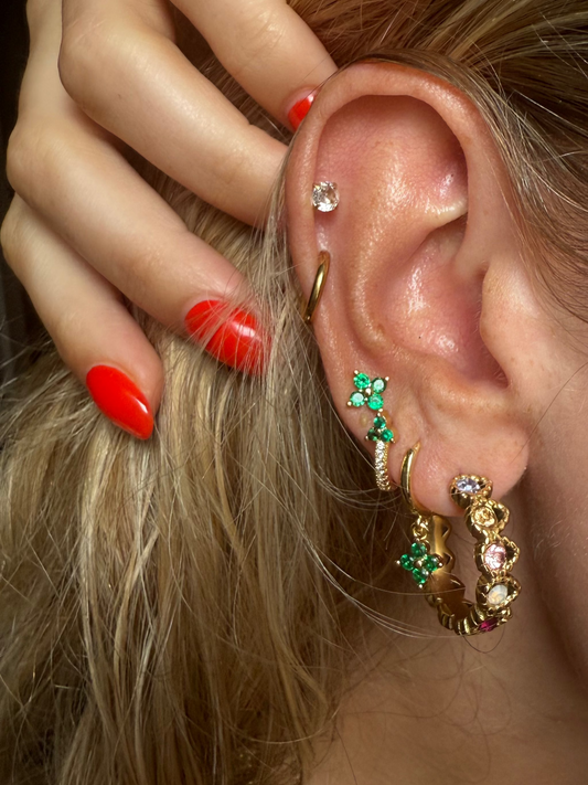 Close-up of an ear with multiple earrings and a hand adjusting hair.