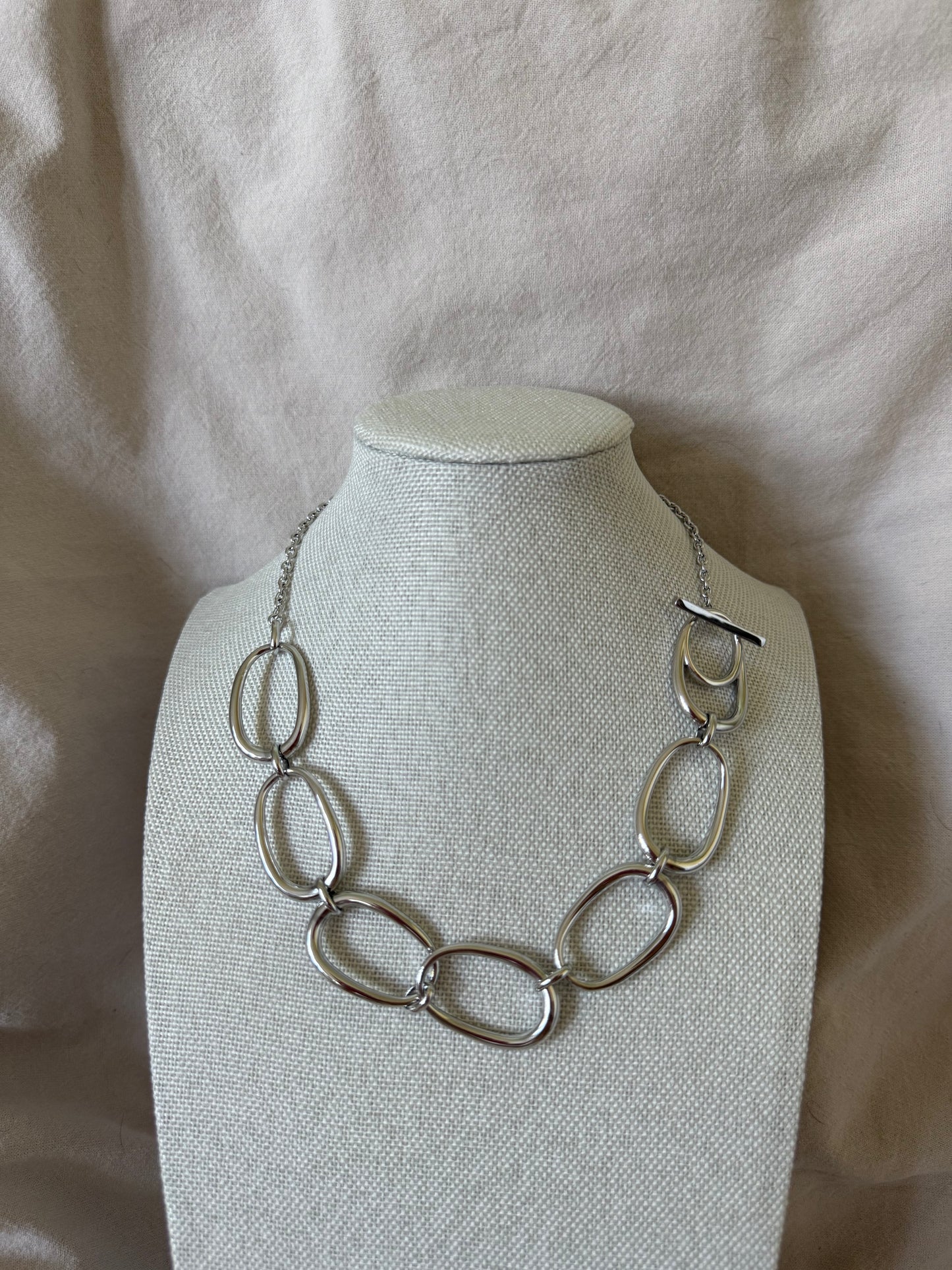 Silver necklace on a white mannequin bust against a beige fabric background